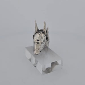 May include: Silver ring with a detailed Anubis head design. The ring is on a clear display stand.