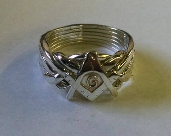 May include: A silver puzzle ring with a Masonic symbol, a compass and square with a 'G' in the center.