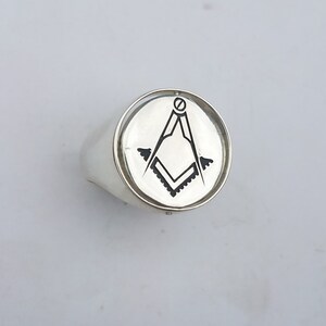 K&ouml;nnte beinhalten: Ein silberner Ring mit einer runden Oberfl&auml;che, auf der ein schwarz-wei&szlig;es, eingraviertes freimaurerisches Symbol, ein Zirkel und ein Winkelma&szlig;, abgebildet sind.