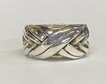 May include: A silver puzzle ring with a complex interwoven design. The ring is made of multiple pieces that are intricately linked together.
