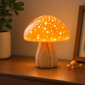 May include: A mushroom-shaped table lamp with a smooth, light-colored wooden base and a glossy, bright orange cap featuring numerous small, circular cutouts that allow light to shine through, creating a glowing, dotted illumination effect.