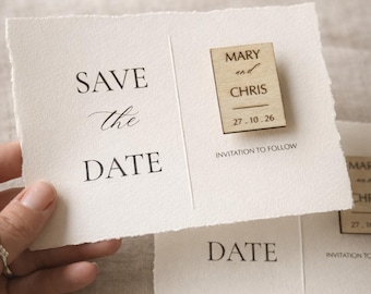 May include: A cream-colored 'Save the Date' card with the text 'SAVE the DATE' in black. A small wooden block with the names 'MARY and CHRIS' and the date '27.10.26' is attached. The words 'INVITATION TO FOLLOW' are also printed.