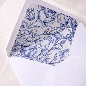 May include: White envelope with a blue floral pattern lining. The floral design features detailed illustrations of roses and leaves. The envelope is open, revealing the patterned interior. The image is a close-up shot.