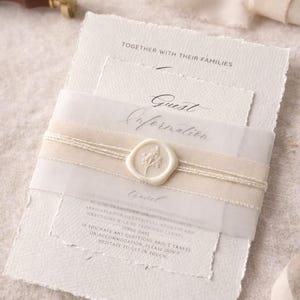 Könnte beinhalten: Cremefarbenes Hochzeitskarten-Set mit strukturiertem Papier und einem Wachssiegel. Die Einladung enthält den Text "TOGETHER WITH THEIR FAMILIES" und "Guest Information". Ein cremefarbenes Band und Bindfaden umwickeln die Einladung.