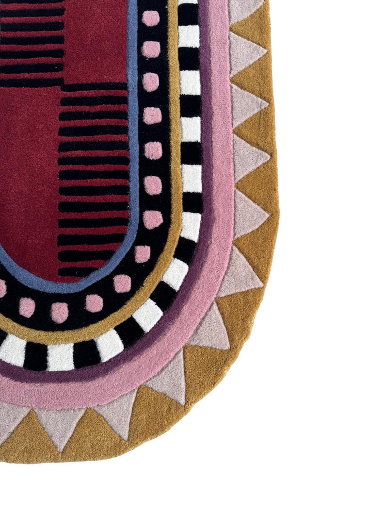 K&ouml;nnte beinhalten: Ein farbenfroher, abstrakter Teppich mit halbkreisf&ouml;rmiger Form. Der Teppich zeigt eine Kombination aus geometrischen Mustern und Formen in Rot-, Schwarz-, Rosa-, Blau-, Wei&szlig;- und Goldt&ouml;nen. Das Design umfasst Streifen, Punkte und Dreiecke.