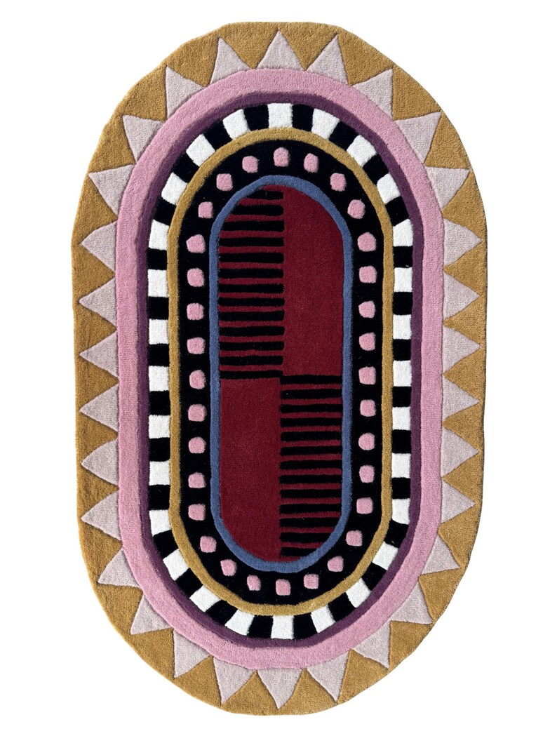 K&ouml;nnte beinhalten: Ovaler Teppich mit geometrischem Muster in Rosa, Gold, Schwarz, Wei&szlig; und Burgunderrot. Das Design umfasst Dreiecke, Streifen und gepunktete Linien, was einen modernen und k&uuml;nstlerischen Look erzeugt. Geeignet f&uuml;r Wohn- oder Schlafzimmer.