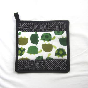 May include: Black and white pot holder with a green turtle pattern. The pot holder has a black border and a white background with green turtles.