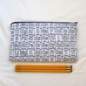 May include: A white pencil case with a black zipper and a repeating pattern of the periodic table of elements. Three yellow pencils are in front of the case.