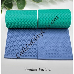 May include: Two teal rolling pins and two blue clay mats with a mermaid scale pattern. The rolling pins are cylindrical and the mats are square. The text "CaliLuciaCo.com" is visible on the mats, and the text "Smaller Pattern" is below the mats.
