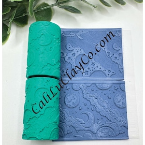 May include: A teal clay roller and a blue clay stamp with a celestial design. The roller has a repeating pattern of moons, clouds, and stars. The stamp features a similar design with the text "CaliLuciaCo.com".