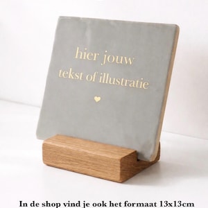 May include: A personalised grey tile, approximately 10x10 cm, displayed on a wooden stand. The tile features gold text that reads "hier jouw tekst of illustratie" with a small heart. The text "Tile 10x10 personalized" is at the top.