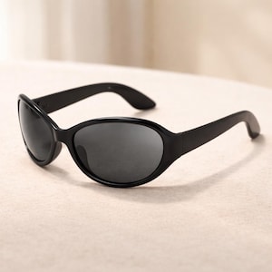 May include: Black sunglasses with oval lenses and a thick, curved frame. The sunglasses have a sleek, modern design, with dark lenses and a matte finish. The arms curve gently, providing a comfortable fit. These sunglasses are suitable for both men and women.