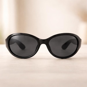 May include: Black oval sunglasses with dark lenses. The sunglasses have a thick, rounded frame and a classic, timeless design. The lenses are dark, providing shade and protection from the sun.