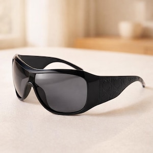 May include: Black sunglasses with a wraparound design. The sunglasses have dark gray lenses and a thick, glossy black frame. The temples feature a textured pattern.
