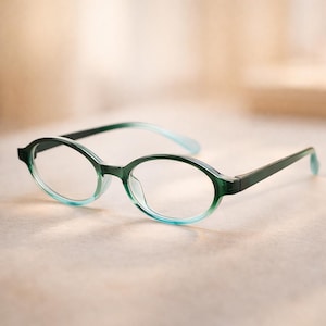 May include: Oval-shaped eyeglasses with a gradient green and blue frame. The lenses are clear, and the temples are a solid dark green. The glasses are set against a neutral background.