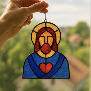 May include: A stained glass artwork depicting Jesus, featuring a yellow halo, red beard, and blue robe. A red heart is centered on the chest. The piece is suspended by a chain. The background shows a blurred green landscape.