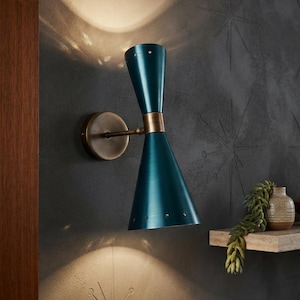 May include: A dual-cone wall sconce featuring a deep teal finish with a metallic brass center connector and a circular wall mount. The lamp emits light from both the top and bottom cones, which are accented with small perforations along the edges.