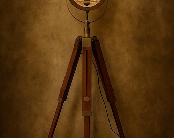 Może przedstawiać: Lampa podłogowa z okrągłą metalową głowicą reflektora z ochronną kratką i świecącą żarówką, zamontowana na trójnożnym drewnianym statywie z regulowanymi metalowymi akcentami i czarnym przewodem zasilającym.