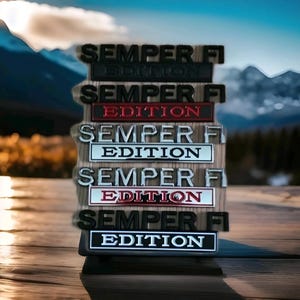 May include: A collection of six metal badges, each displaying the text "SEMPER FI EDITION". The badges, in different colours, are mounted on a wooden block, set against a mountain and lake backdrop.