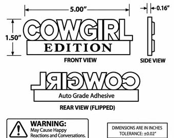 Peut inclure: Un schéma technique en noir et blanc d'un emblème COWGIRL EDITION. La vue de face indique des dimensions de 5,00 pouces sur 1,50 pouces, et la vue latérale montre une épaisseur de 0,16 pouces. La vue arrière indique Auto Grade Adhesive. Inclut une étiquette d'avertissement.