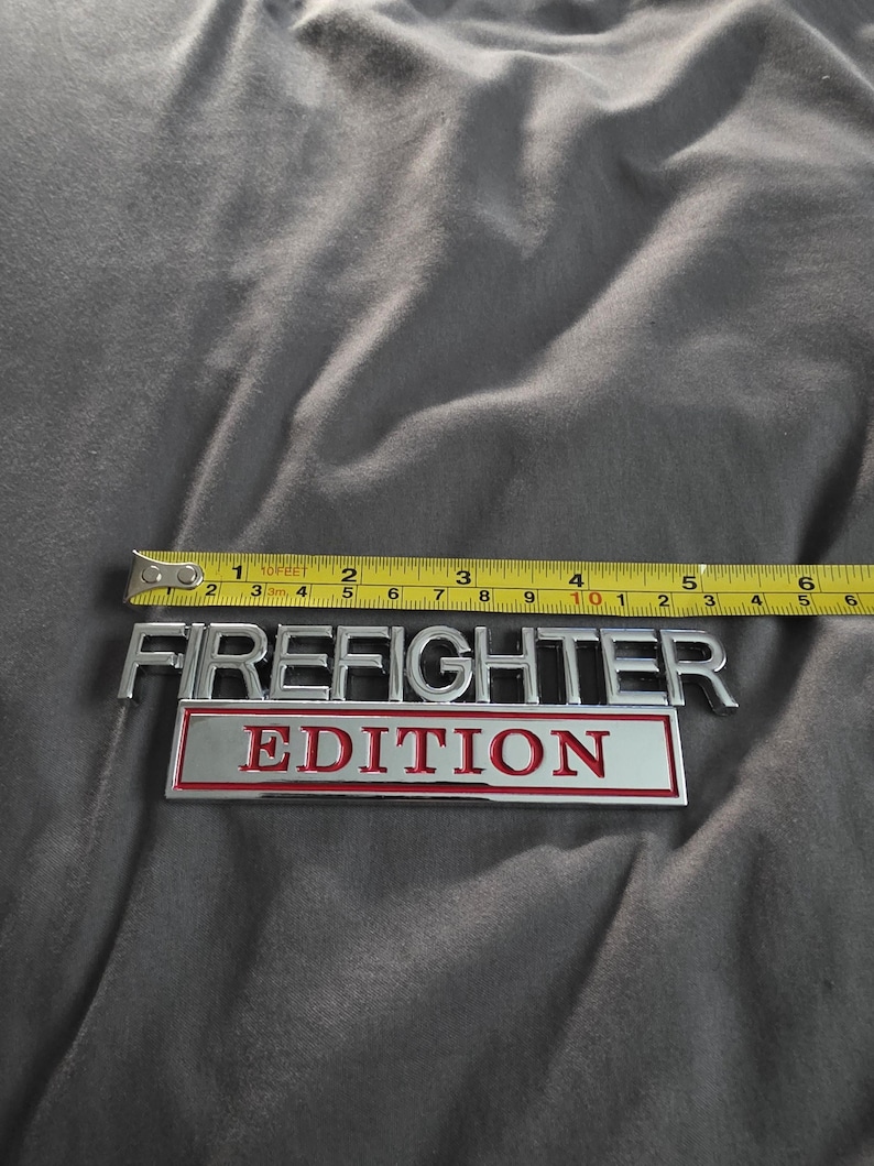 以下が含まれることがあります： 約12.7cmのクロムと赤色の「FIREFIGHTER EDITION」エンブレムが表示されています。エンブレムは黄色の巻尺で測定されています。テキストは太字のサンセリフ体です。
