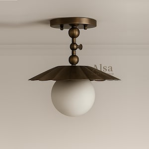 Könnte beinhalten: Eine Deckenleuchte mit Bronze-Finish. Sie verfügt über einen gewellten Schirm, ein weißes kugelförmiges Licht und einen dekorativen Stiel. Die Leuchte ist für den Innenbereich konzipiert und verleiht jedem Raum einen Hauch von Vintage-Charme.