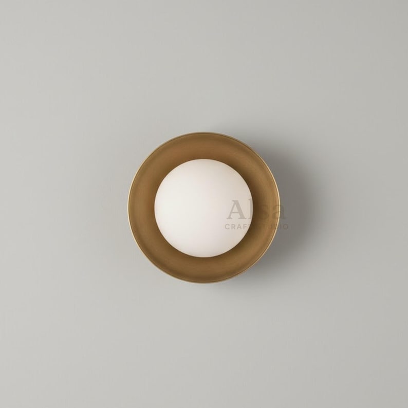 Minimalist brass wall lamp with circular backplate and soft glow