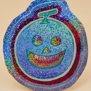 May include: A circular sticker featuring a stylized melon with a jack-o'-lantern face. The design has a light blue base with purple line details, a green stem, and a holographic finish that reflects rainbow colors across the surface.