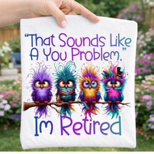 Peut inclure: T-shirt blanc avec une illustration colorée de quatre hiboux fantaisistes perchés sur une branche. Les hiboux sont dans des tons de violet, bleu, jaune et rose. Le texte sur le t-shirt se lit "That Sounds Like A You Problem. I'm Retired."