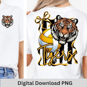 May include: White t-shirt featuring a tiger head graphic on the front and a volleyball design with the word "Tigers" on the back. The tiger design is orange, black, and white. The volleyball is yellow, white, and blue.