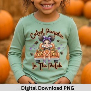 Può includere: Una maglietta verde chiaro a maniche lunghe con una grafica di una ragazza su un camion arancione pieno di zucche. Il testo sulla maglietta recita "Cutest Pumpkin In The Patch".
