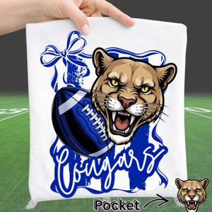 Cougars Football PNG design featuring fierce cougar mascot in bold blue and white team colors with football graphic, including front or back layout and coordinating pocket design. High resolution sports mascot clipart with transparent background for football game day shirts, school spirit apparel, football mom tees, pep rally outfits, and fall team merchandise.