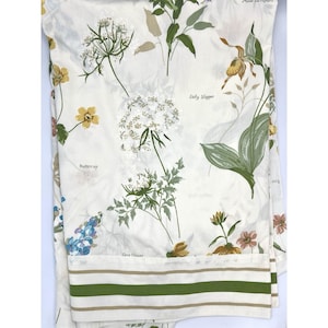 May include: White fabric printed with botanical illustrations of flowers, including buttercups and lady slippers. The fabric has green and beige stripes at the bottom. The names of the flowers are printed on the fabric.