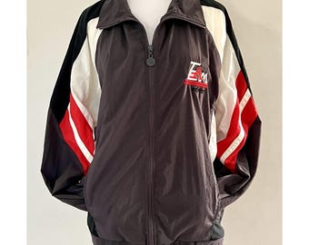 May include: A dark brown zip-up jacket with black and white accents. The jacket features red stripes on the sleeves and the text "EAM" in white and red on the chest. The jacket has a high collar and a full zipper.