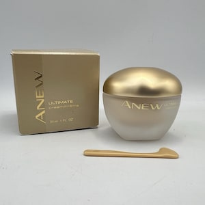 Könnte beinhalten: Ein goldfarbener Tiegel mit ANEW Ultimate Creme, passendem Deckel und kleinem Applikator. Das Produkt befindet sich in einer goldenen Schachtel mit dem ANEW-Logo und Produktinformationen. Der Tiegel enthält 30 ml Creme.