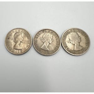 May include: Three silver coins featuring a profile of a woman, with text around the edges. The coins are arranged horizontally against a light background. The text includes "REGINA", "ELIZABETH", and "DEI GRATIA".