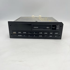 May include: A white ceramic mug with a black handle and the text "But First, Coffee" in a black, bold font. The mug is sitting on a wooden surface. The mug is approximately 4 inches tall.