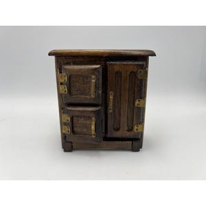 May include: A small wooden fridge with two doors and brass fittings. The upper door is split into two sections. The wood has a dark brown finish. The fridge is a vintage style.