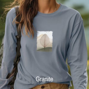 May include: A long-sleeved, granite-colored shirt featuring a rectangular graphic of a leaf skeleton design set against a landscape of rolling hills. The word "Granite" is printed at the bottom of the shirt.