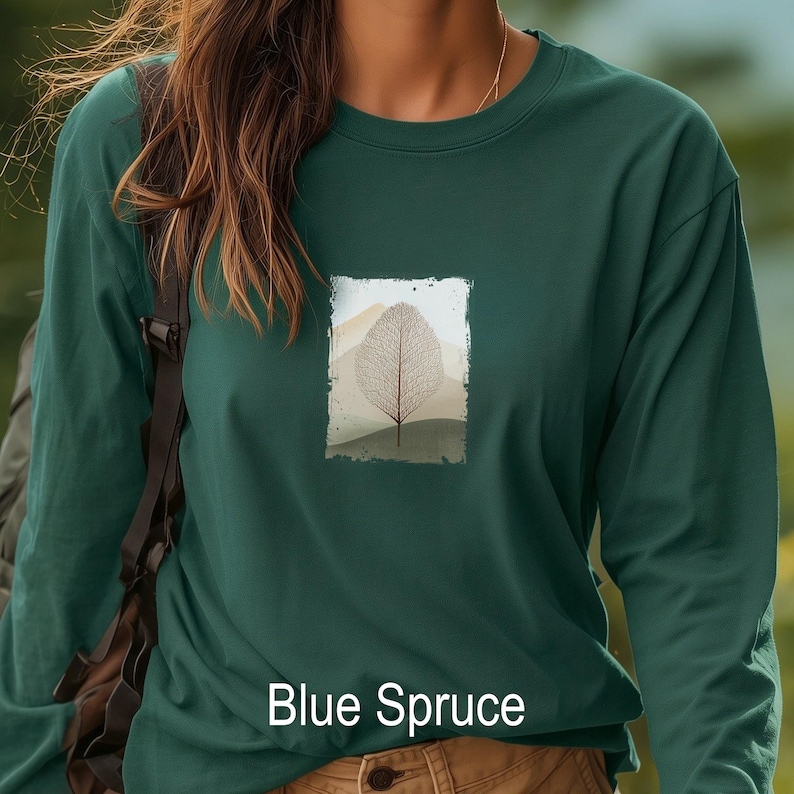 May include: A long-sleeve shirt in blue spruce color. The shirt features a rectangular graphic of a leaf and mountain landscape. The text "Blue Spruce" is printed at the bottom of the shirt.