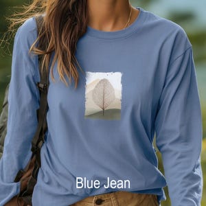 May include: A long-sleeved, blue jean colored shirt. The shirt features a rectangular graphic of a leaf skeleton design with a mountain landscape background. The text "Blue Jean" is printed at the bottom of the shirt.