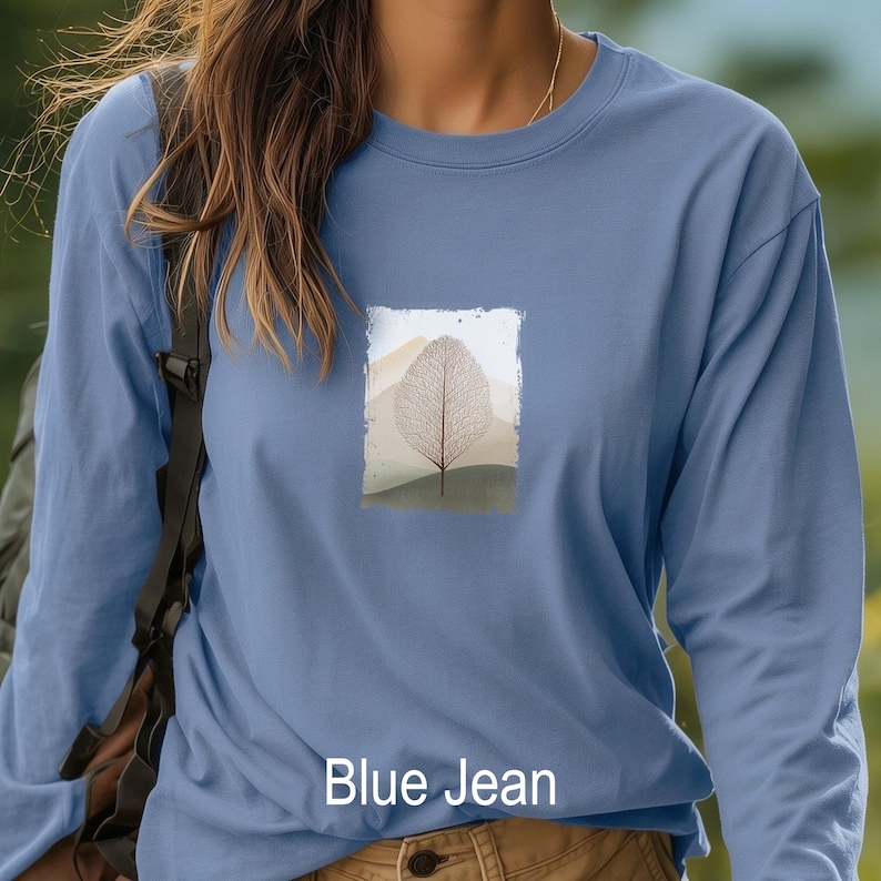 May include: A long-sleeved, blue jean colored shirt. The shirt features a rectangular graphic of a leaf skeleton design with a mountain landscape background. The text "Blue Jean" is printed at the bottom of the shirt.