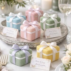 May include: A collection of colorful, crocheted gift boxes with satin ribbon bows. The boxes are in shades of blue, pink, green, lavender, and yellow. Each box has a white ribbon band and a small card that reads "Thank You Bridesmaid."