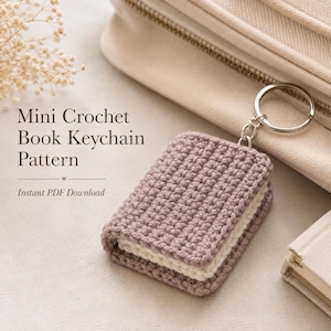 May include: A handmade crochet book keychain in shades of mauve and cream, attached to a silver keyring. The keychain is designed to resemble a miniature book. Text on the image reads "Mini Crochet Book Keychain Pattern" and "Instant PDF Download."
