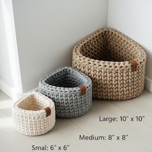 Könnte beinhalten: Drei handgefertigte Häkelkörbe in verschiedenen Größen und Farben. Der kleinste ist cremefarben, der mittlere grau und der größte beige. Jeder Korb hat einen Lederakzent. Größen: Klein: 15 cm x 15 cm, Mittel: 20 cm x 20 cm und Groß: 25 cm x 25 cm.