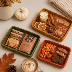 Op de afbeelding: Drie rechthoekige gehaakte dienbladen in mosterdgeel, bosgroen en oranje. Het groene dienblad bevat Bigelow Pumpkin Spice en Yogi Chai Rooibos theezakjes. Het gele dienblad bevat een kaars, kaneelstokjes, gedroogde sinaasappelschijfjes en cacaopakketjes. Het oranje dienblad bevat maissnoepjes, pompoensnoepjes en blaadjesvormige chocolaatjes.