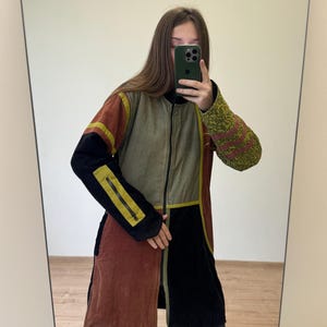 May include: A patchwork coat in shades of brown, black, olive green, and gold. The coat features a zip-up front, long sleeves, and a unique design with contrasting panels. The sleeves have a decorative pattern. The coat is knee-length.