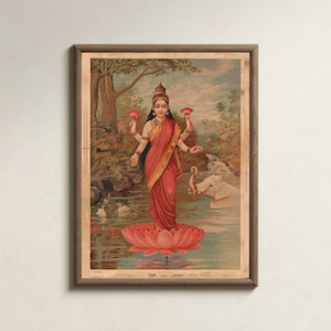May include: A framed print of a Hindu goddess standing on a lotus flower in a river. The goddess wears a red sari and holds lotus flowers. An elephant is in the water. The background features trees and a cloudy sky.