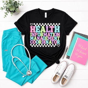 May include: Black t-shirt with the text "HEALTH INFORMATION MANAGEMENT COORDINATOR" in pastel colors. The shirt is paired with teal scrubs, a stethoscope, white sneakers, and notebooks. A small potted plant is in the background.