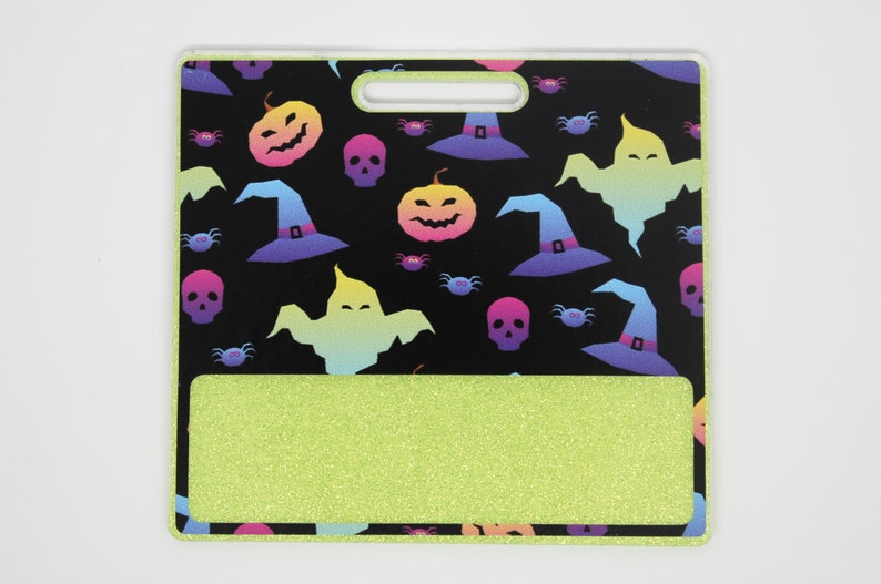 K&ouml;nnte beinhalten: Ein Ausweishalter zum Thema Halloween mit schwarzem Hintergrund und einem sich wiederholenden Muster aus bunten K&uuml;rbissen, Hexenh&uuml;ten, Geistern, Totenk&ouml;pfen und Spinnen. Der untere Bereich ist glitzernd limettengr&uuml;n und hat einen Griff.